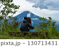 A couple of lovers are sitting on a bench, hugging each other and enjoying the view of the popular sacred cloud-covered Mount Agung on the island of Bali. 130713431