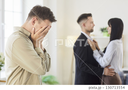 Upset man emotionally reacts to romantic couple embracing closely in bright room Upset man emotionally reacts to romantic couple embracing closely in bright room 130713554