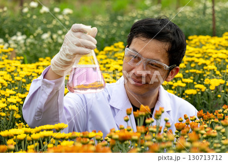 Scientist in protective gloves and safety glasses holding flask with purple liquid in flower field, symbolizing agricultural research, biotechnology, plant science, eco innovation, and sustainable 130713712