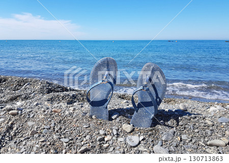 Blue flip flops on a pebble beach by the sea, summer waves and copy space 130713863