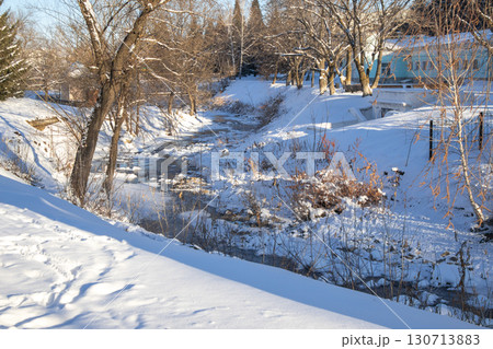 Urban creek in winter with snow and ice, shadows on the park bank 130713883
