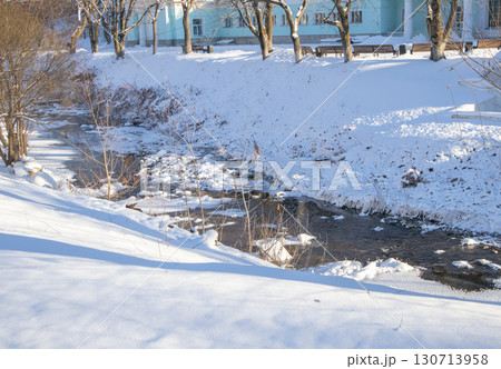 Urban creek in winter with snow and ice, shadows on the park bank 130713958