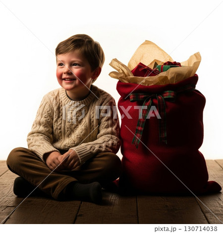 Smiling Boy Sitting Beside Red Christmas Sack Full of Presents on Wood Floor 130714038