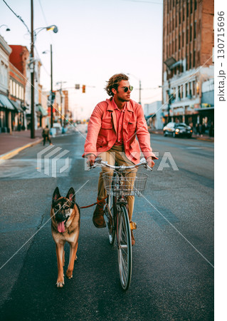 A man in a pink jacket rides a bicycle with a dog on a leash A man in a pink jacket rides a bicycle with a dog on a leash 130715696
