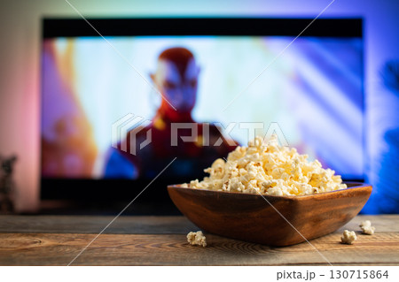 A wooden bowl of popcorn and remote control in the background the TV works. Evening cozy watching a movie or TV series at home 130715864