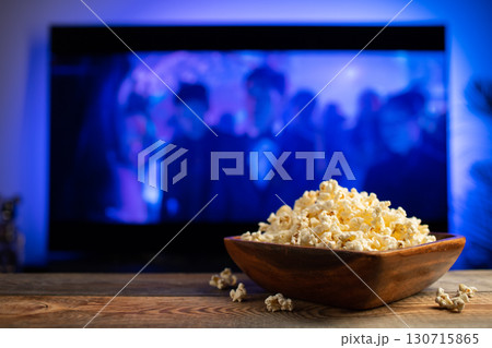 A wooden bowl of popcorn and remote control in the background the TV works. Evening cozy watching a movie or TV series at home 130715865