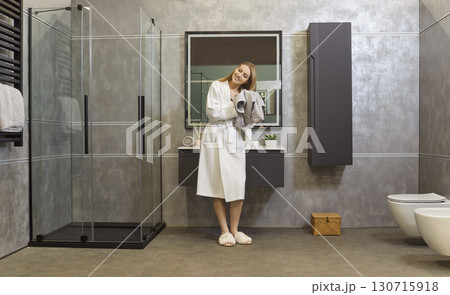 Woman in bathrobe drying hair with towel standing in bathroom interior after taking shower. 130715918
