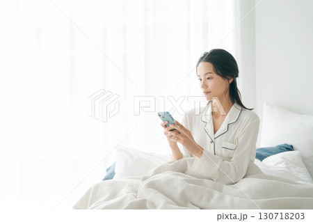 ベッドでスマホを操作する女性 ベッドでスマホを操作する女性 130718203