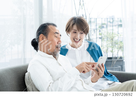 ソファでスマホを見るシニア夫婦 130720692