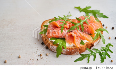 Open sandwich with smoked salmon, cream cheese, arugula, and pepper on crusty bread. Tasty fresh snack on light background. Top view. Open sandwich with smoked salmon, cream cheese, arugula, and pepper on crusty bread. Tasty fresh snack on light background. Top view. 130721628