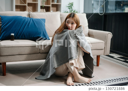 Young Asian woman suffering from flu symptoms, covered with a blanket on a sofa. Concept of illness, healthcare, and recovery. Young Asian woman suffering from flu symptoms, covered with a blanket on a sofa. Concept of illness, healthcare, and recovery. 130721886