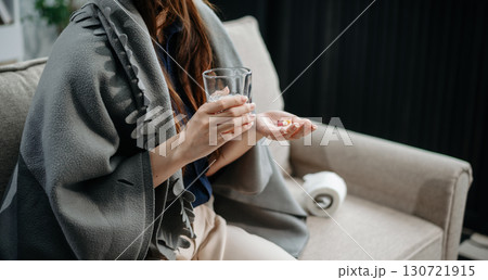 Young Asian woman suffering from flu symptoms, covered with a blanket on a sofa. Concept of illness, healthcare, and recovery. Young Asian woman suffering from flu symptoms, covered with a blanket on a sofa. Concept of illness, healthcare, and recovery. 130721915