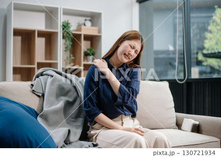 Young Asian woman suffering from flu symptoms, covered with a blanket on a sofa. Concept of illness, healthcare, and recovery. Young Asian woman suffering from flu symptoms, covered with a blanket on a sofa. Concept of illness, healthcare, and recovery. 130721934