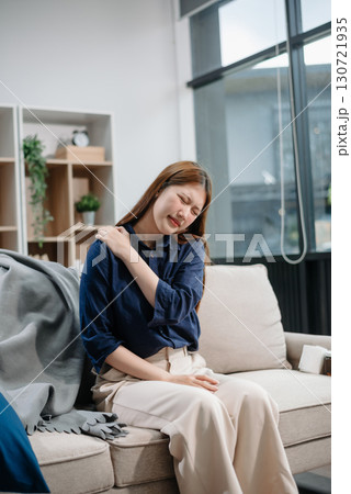 Young Asian woman suffering from flu symptoms, covered with a blanket on a sofa. Concept of illness, healthcare, and recovery. Young Asian woman suffering from flu symptoms, covered with a blanket on a sofa. Concept of illness, healthcare, and recovery. 130721935