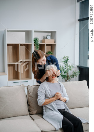 Happy adult Asian granddaughter and senior grandmother having fun enjoying talk sit on sofa in modern living room, using a laptop, tablet 130721994