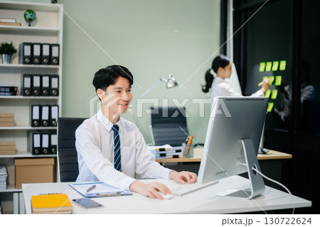 Two young Asian professionals engaged in teamwork and business discussions in modern office embodying corporate Two young Asian professionals engaged in teamwork and business discussions in modern office embodying corporate 130722624