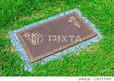 Bronze memorial marker with floral engravings cross rests on peaceful cemetery 130723509