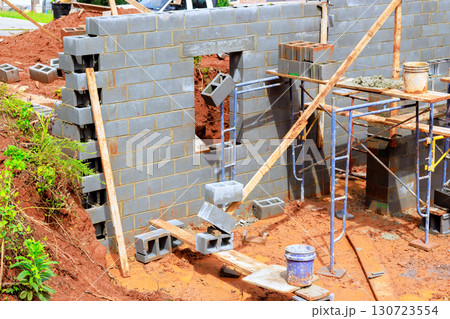 Workers lay blocks for new structure while using scaffolding, tools at construction site during works day. 130723554
