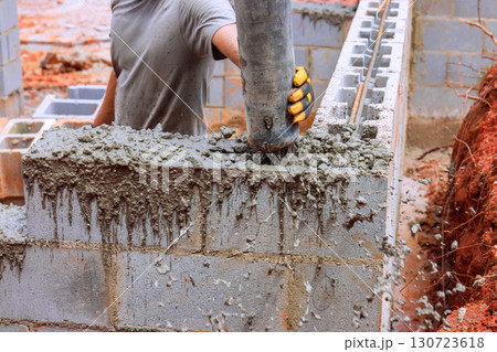 Construction worker skillfully fills concrete into blocks while building structure on works day outdoors. Construction worker skillfully fills concrete into blocks while building structure on works day outdoors. 130723618