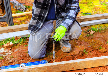 Worker uses tool to dig while kneeling on ground, ensuring proper alignment at construction site. 130723619