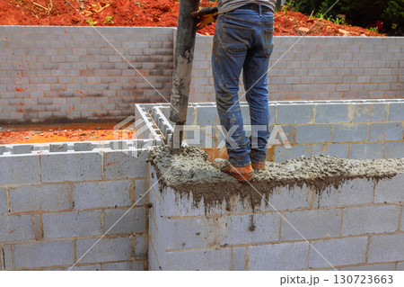 Construction worker pours cement to create sturdy walls at building site during works day. 130723663