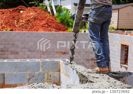 Concrete is being poured by worker into foundation wall at construction site under works day Concrete is being poured by worker into foundation wall at construction site under works day 130723692
