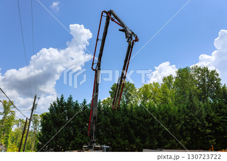 Concrete pump truck stands tall against bright blue sky while workers prepare construction site in background. Concrete pump truck stands tall against bright blue sky while workers prepare construction site in background. 130723722
