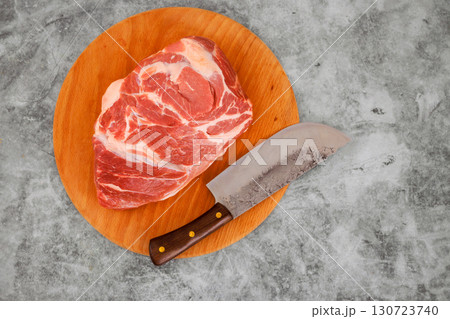 Raw pork shoulder sits on wooden cutting board next to shiny knife, ready for preparation in home kitchen. Raw pork shoulder sits on wooden cutting board next to shiny knife, ready for preparation in home kitchen. 130723740
