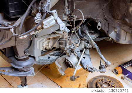 Mechanics work on exposed suspension parts, surrounded by tools in garage, indicating an ongoing vehicle repair. 130723742