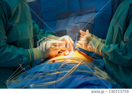 Male and female surgeons focus intensely while performing surgery in operating room. Medical instruments surround them, creating a serious atmosphere. 130723759