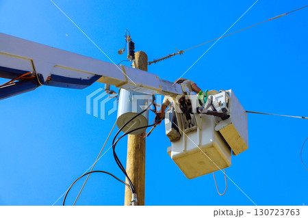 Electrical technicians in bucket lift conduct maintenance on utility pole under bright blue sky. Electrical technicians in bucket lift conduct maintenance on utility pole under bright blue sky. 130723763