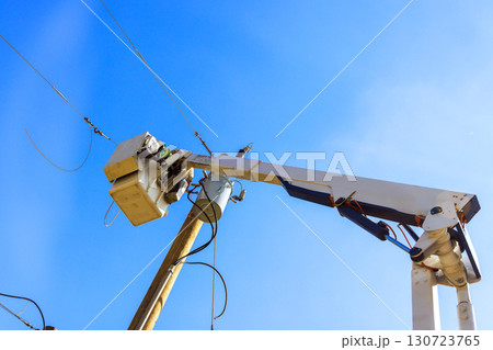 Utility workers are repairing electrical lines from cherry picker under bright blue sky. Utility workers are repairing electrical lines from cherry picker under bright blue sky. 130723765