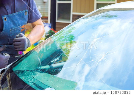 Technician works on damaged windshield from vehicle parked in suburban driveway on replace windshield 130723853