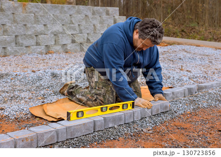 Worker carefully aligns stones while building pathway on gravel surface during work day Worker carefully aligns stones while building pathway on gravel surface during work day 130723856