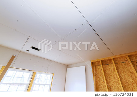 Drywall being installed in residential room, with visible seams natural light coming through windows. Drywall being installed in residential room, with visible seams natural light coming through windows. 130724031
