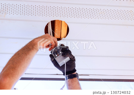 An individual in gloves is attaching fixture inside ceiling hole, using tool in well lit indoor space. 130724032