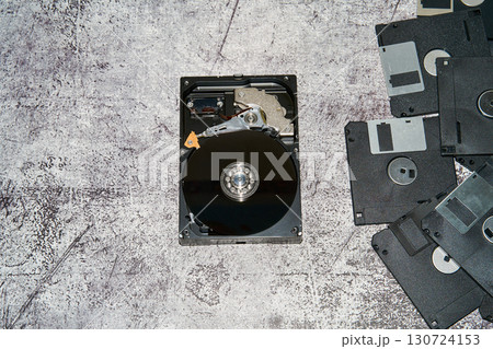 An open 3.5 inch hard disk drive alongside multiple floppy disks on a gray surface. 130724153
