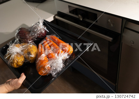 Hand Placing Vegetables Wrapped For Baking Into A Kitchen Oven Hand Placing Vegetables Wrapped For Baking Into A Kitchen Oven 130724742