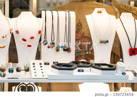 Handcrafted glass jewelry including earrings, necklaces, rings, and pendants arranged in a boutique window display. Intentional design, meaningful luxury, artisan craftsmanship, anti-mass production 130725658