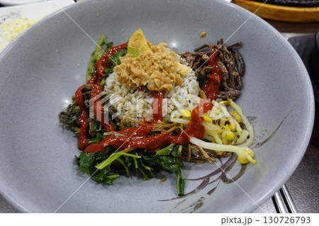 Bibimbap, a vibrant Korean rice dish topped with a variety of seasoned vegetables, gochujang, and a fried egg, often accompanied by sliced meat. Mixed together, it creates a flavorful and balanced. 130726793