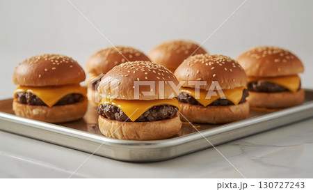 Group of cheeseburgers with grilled beef patties, melted cheddar cheese, and sesame seed buns arranged on tray. Tasty fast food treat for National Cheeseburger Day. 130727243