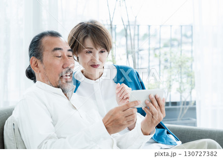 ソファでスマホを見るシニア夫婦 130727382