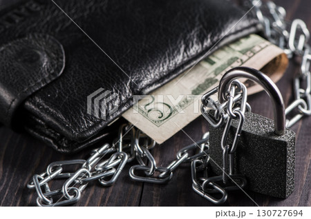 The wallet with money is tightly clamped in a metal chain, symbolizing control and restriction 130727694
