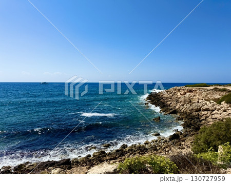 Picturesque beach, waves crashing on the sandy shore. Sea waves beat against the rocks. Cyprus Island, umbrellas, tourist boats, Mediterranean Sea. 130727959