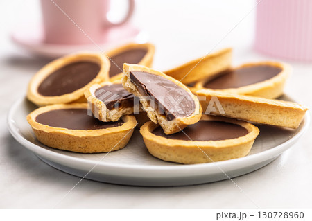 Sweet chocolate tartelettes on plate on white table. Sweet chocolate tartelettes on plate on white table. 130728960