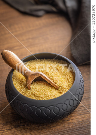 Uncooked couscous in bowl on wooden table. 130728970