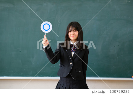 クイズに答える女子学生　学校の教室で○✕を出す教育イメージ 130729285