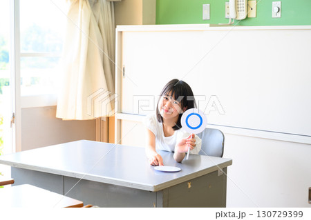 クイズに答える女子学生　学校の教室で○✕を出す教育イメージ 130729399