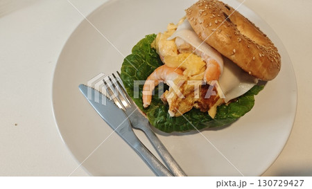 Bagel sandwich with scrambled eggs, shrimp, cheese, and lettuce served on a white plate 130729427