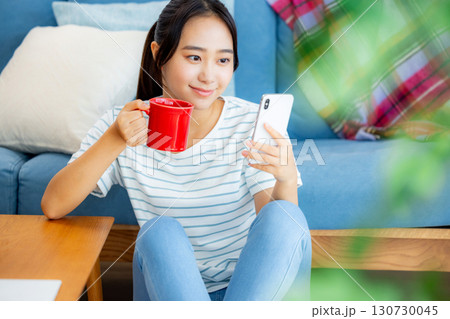 ソファーでくつろぎながらスマホを操作する女性 ソファーでくつろぎながらスマホを操作する女性 130730045